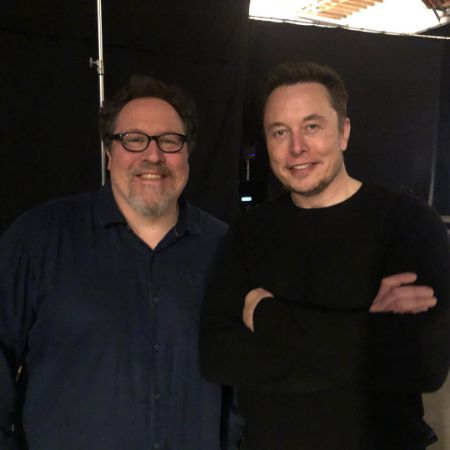 Jon Favreau and Elon Musk are standing next to each other smiling at the camera.